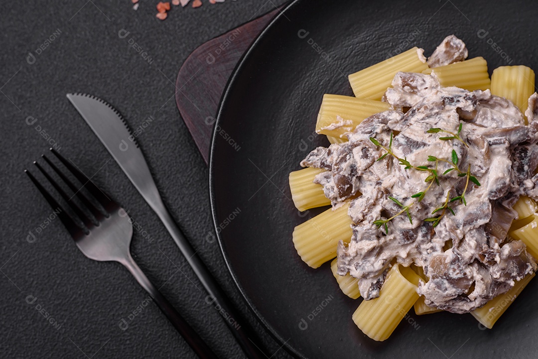 Deliciosa massa fresca com cogumelos champignon em molho cremoso com sal, especiarias e ervas sobre fundo escuro de concreto