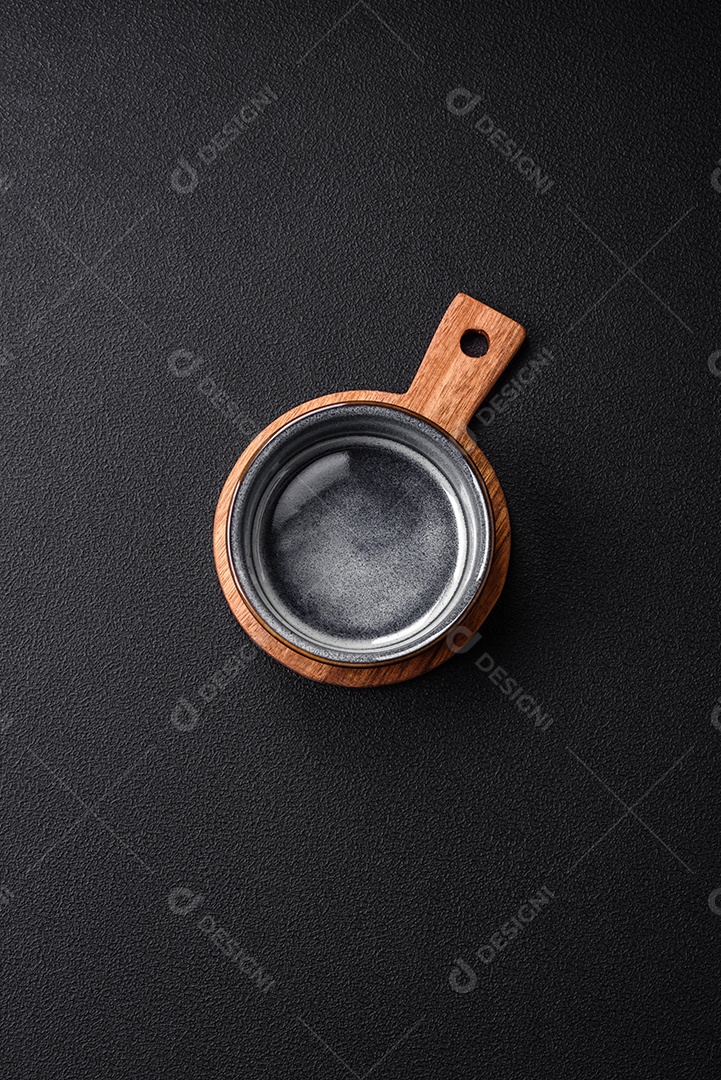 Tigela de cerâmica redonda vazia sobre uma tábua de madeira de cor marrom sobre um fundo de concreto texturizado escuro