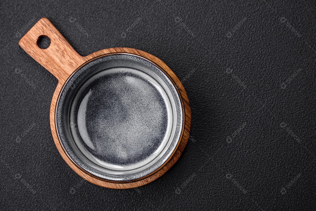 Tigela de cerâmica redonda vazia sobre uma tábua de madeira de cor marrom sobre um fundo de concreto texturizado escuro