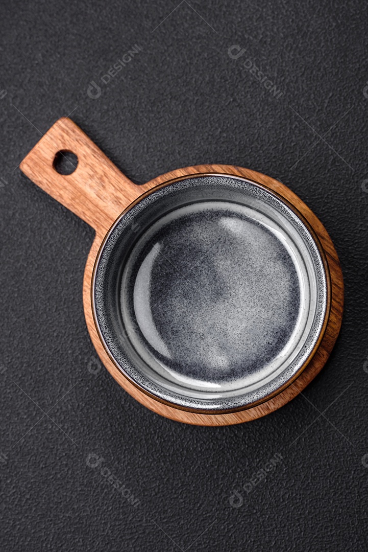 Tigela de cerâmica redonda vazia sobre uma tábua de madeira de cor marrom sobre um fundo de concreto texturizado escuro