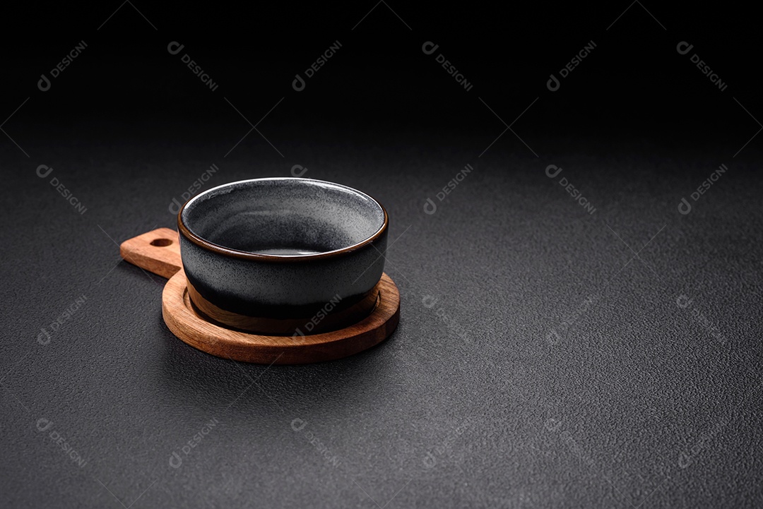 Tigela de cerâmica redonda vazia sobre uma tábua de madeira de cor marrom sobre um fundo de concreto texturizado escuro