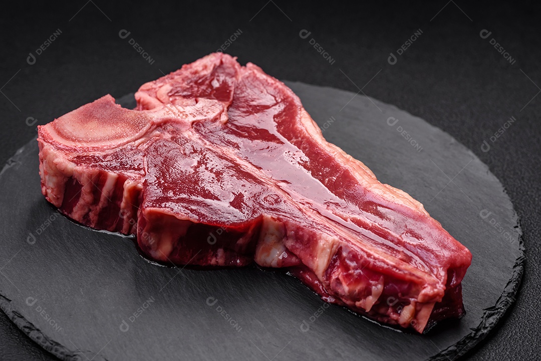 Bife de carne crua e suculenta com sal, especiarias e ervas sobre um fundo escuro de concreto