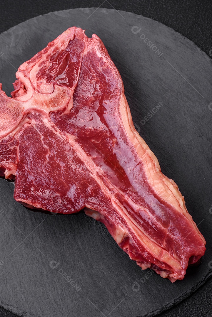 Bife de carne crua e suculenta com sal, especiarias e ervas sobre um fundo escuro de concreto