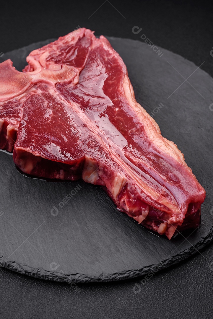Bife de carne crua e suculenta com sal, especiarias e ervas sobre um fundo escuro de concreto