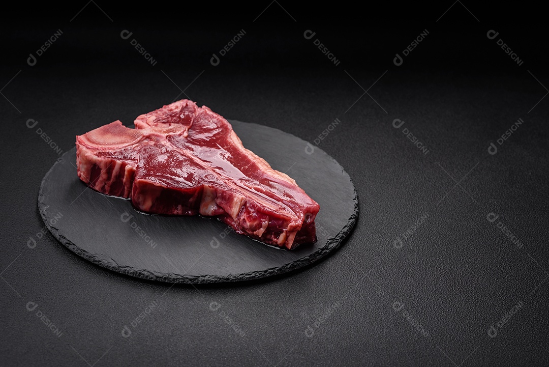 Bife de carne crua e suculenta com sal, especiarias e ervas sobre um fundo escuro de concreto