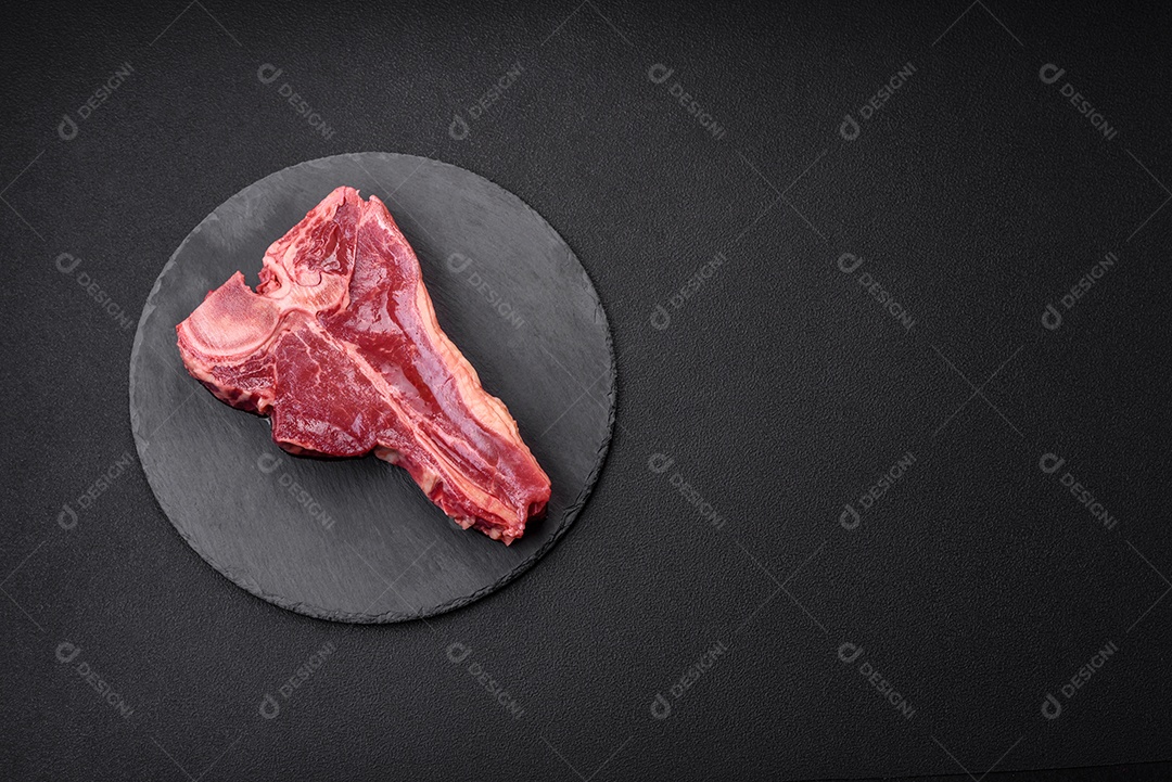 Bife de carne crua e suculenta com sal, especiarias e ervas sobre um fundo escuro de concreto