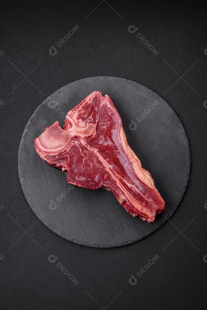 Bife de carne crua e suculenta com sal, especiarias e ervas sobre um fundo escuro de concreto