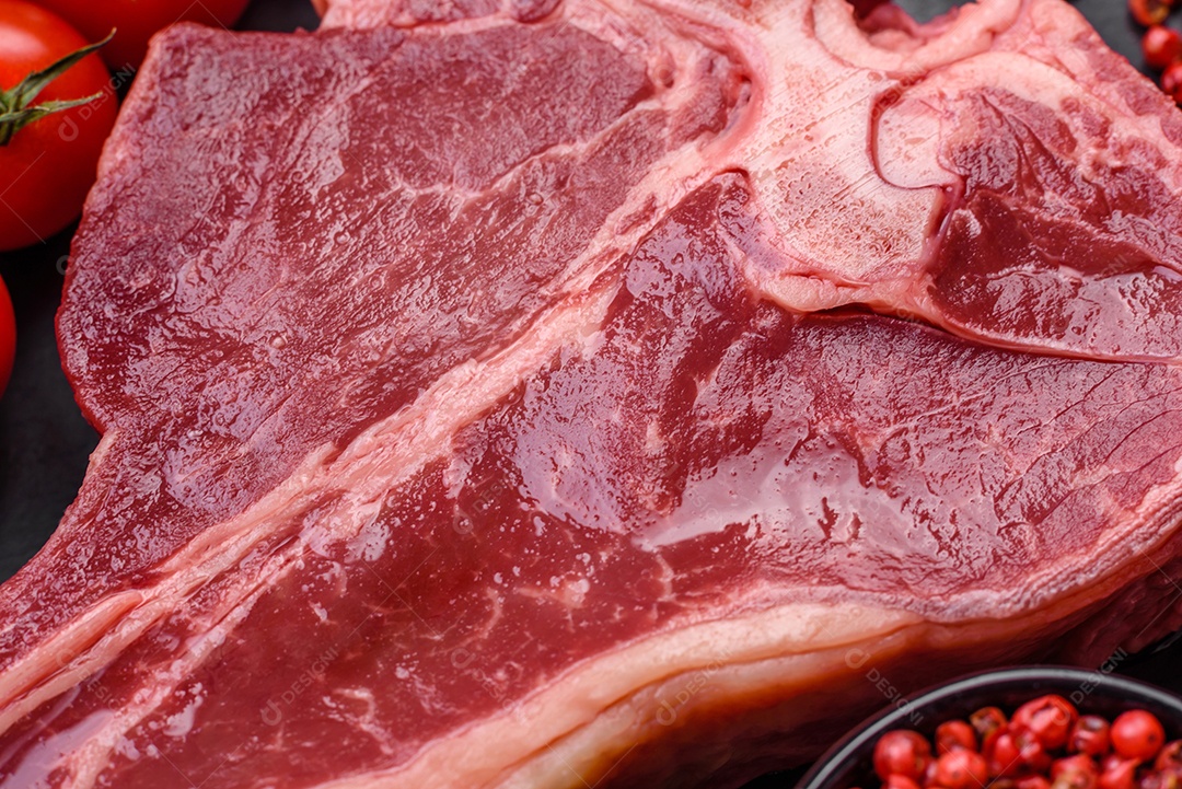 Bife de carne crua e suculenta com sal, especiarias e ervas sobre um fundo escuro de concreto