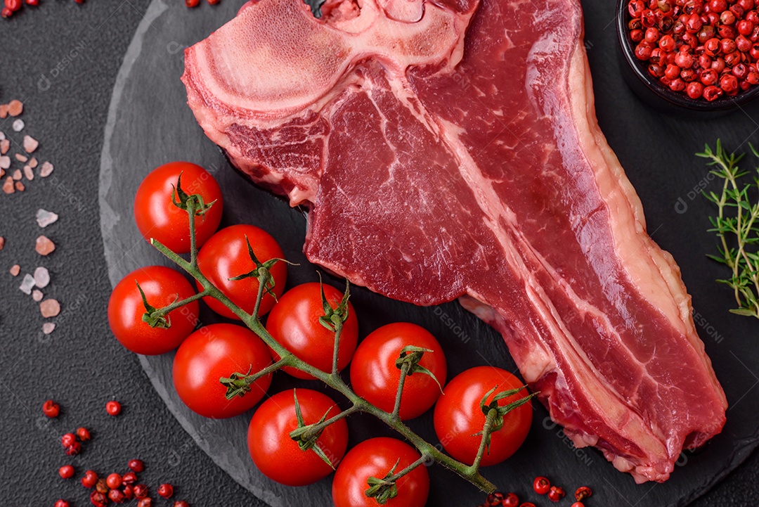 Bife de carne crua e suculenta com sal, especiarias e ervas sobre um fundo escuro de concreto