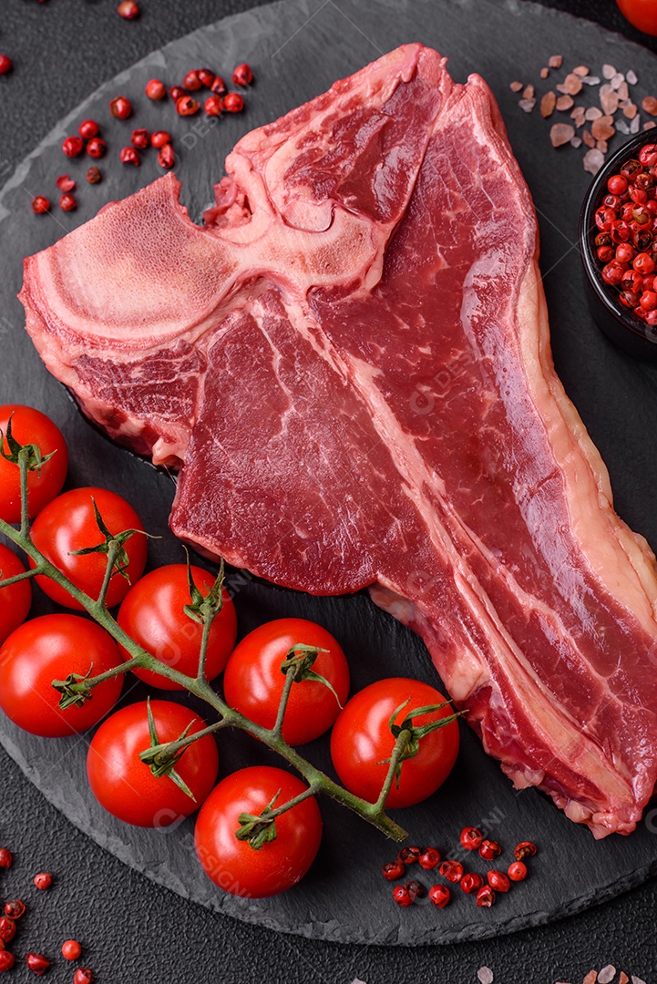 Bife de carne crua e suculenta com sal, especiarias e ervas sobre um fundo escuro de concreto
