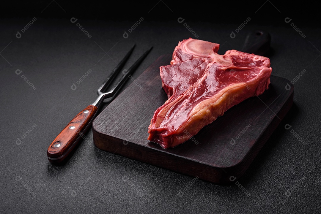 Bife de carne crua e suculenta com sal, especiarias e ervas sobre um fundo escuro de concreto