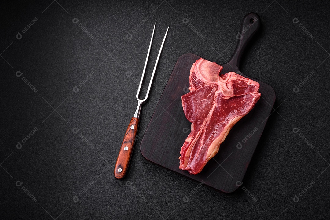 Bife de carne crua e suculenta com sal, especiarias e ervas sobre um fundo escuro de concreto