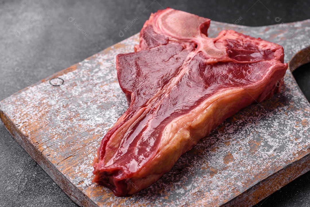 Bife de carne crua e suculenta com sal, especiarias e ervas sobre um fundo escuro de concreto