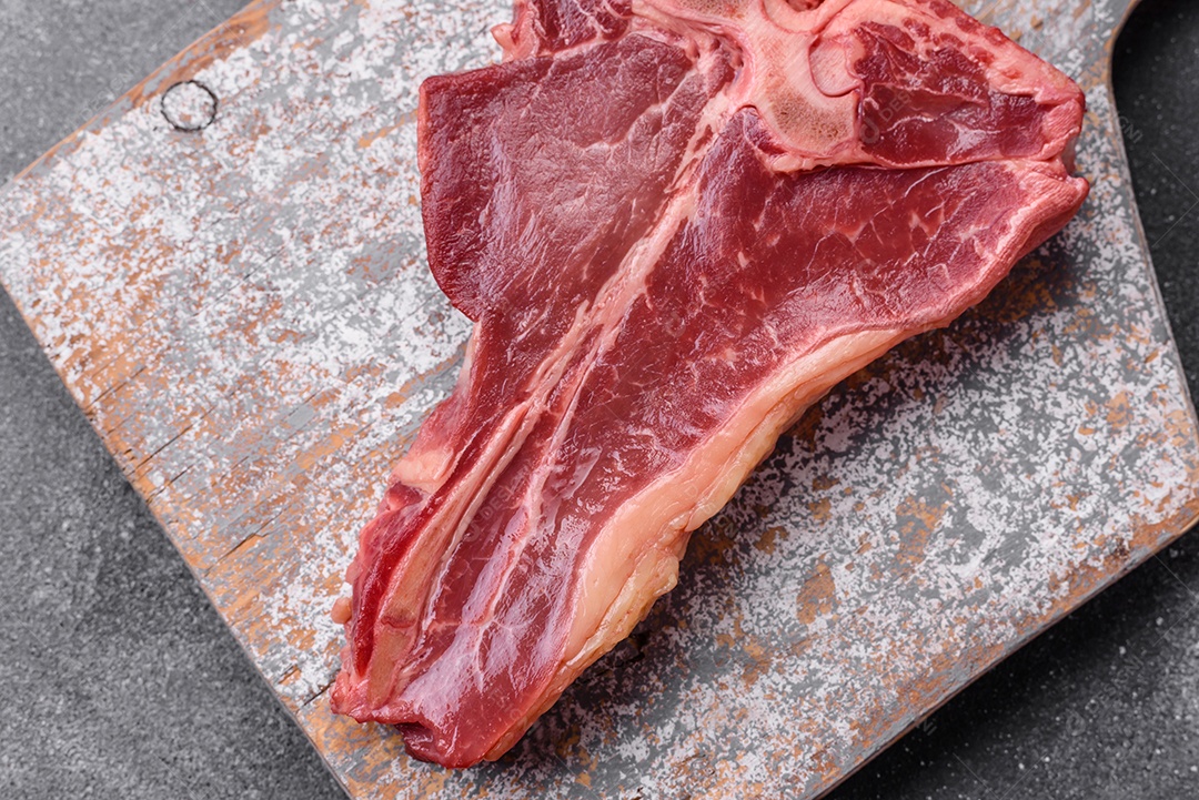 Bife de carne crua e suculenta com sal, especiarias e ervas sobre um fundo escuro de concreto