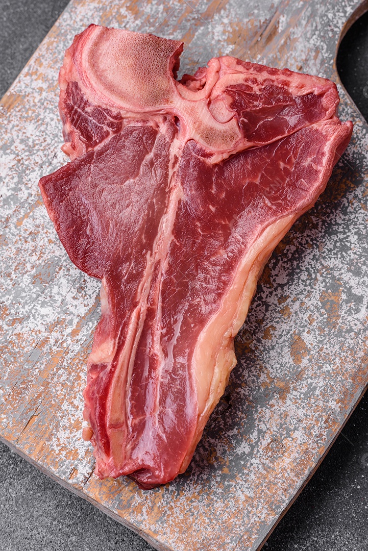 Bife de carne crua e suculenta com sal, especiarias e ervas sobre um fundo escuro de concreto