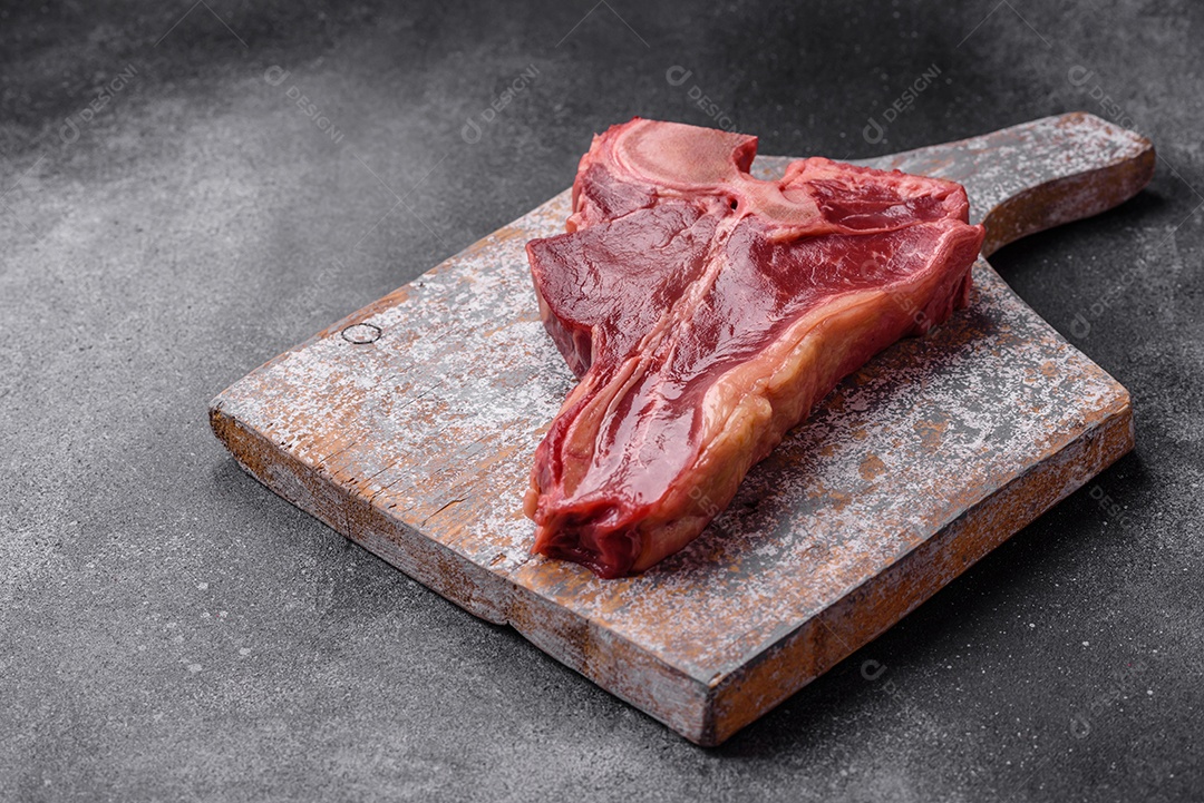 Bife de carne crua e suculenta com sal, especiarias e ervas sobre um fundo escuro de concreto