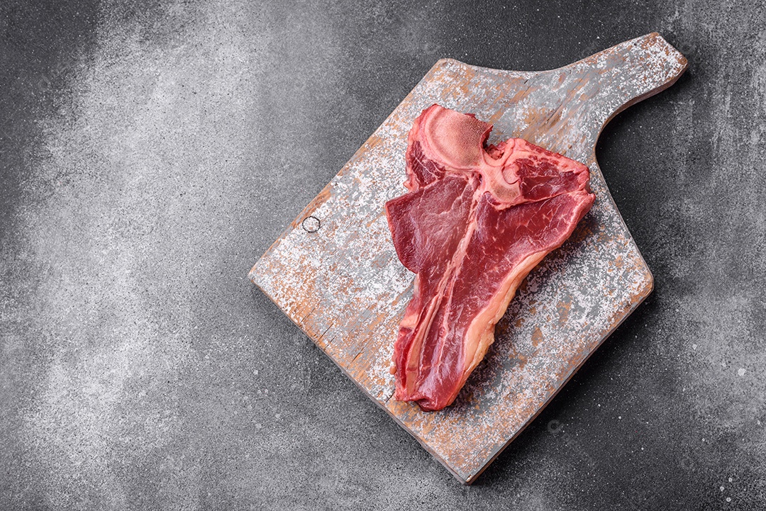 Bife de carne crua e suculenta com sal, especiarias e ervas sobre um fundo escuro de concreto