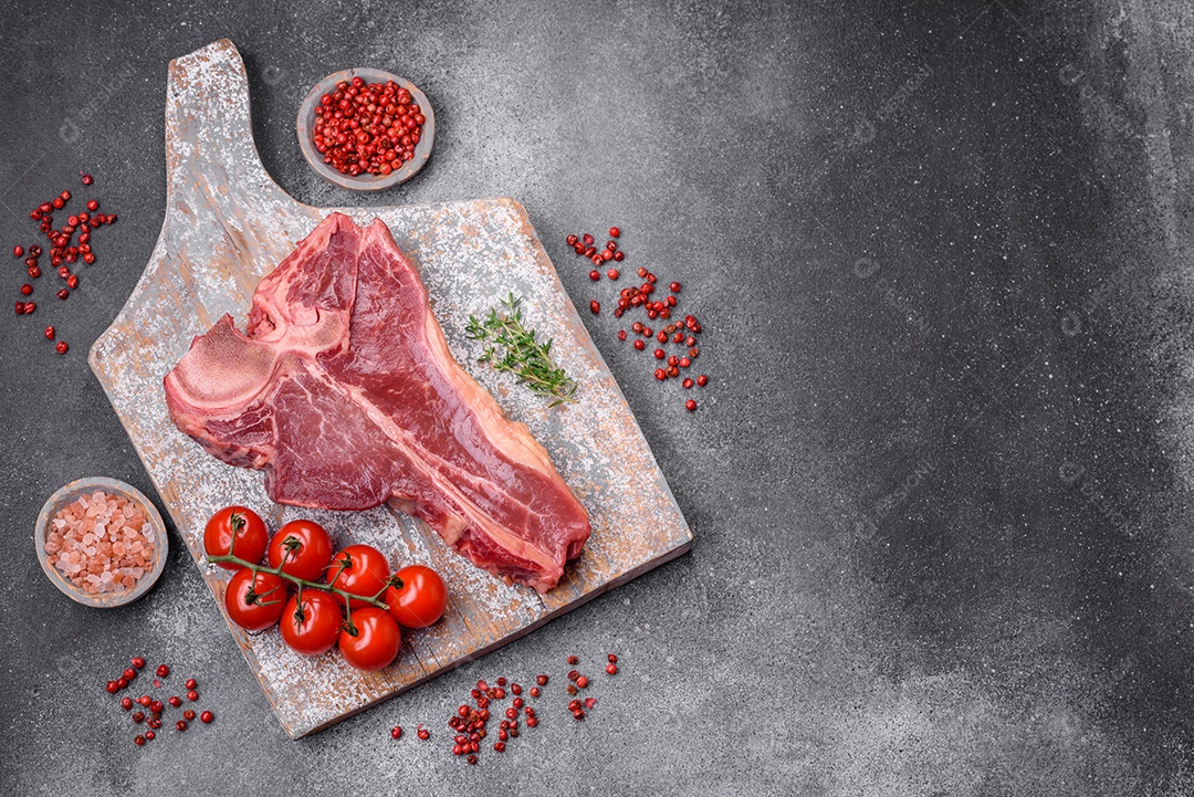 Bife de carne crua e suculenta com sal, especiarias e ervas sobre um fundo escuro de concreto