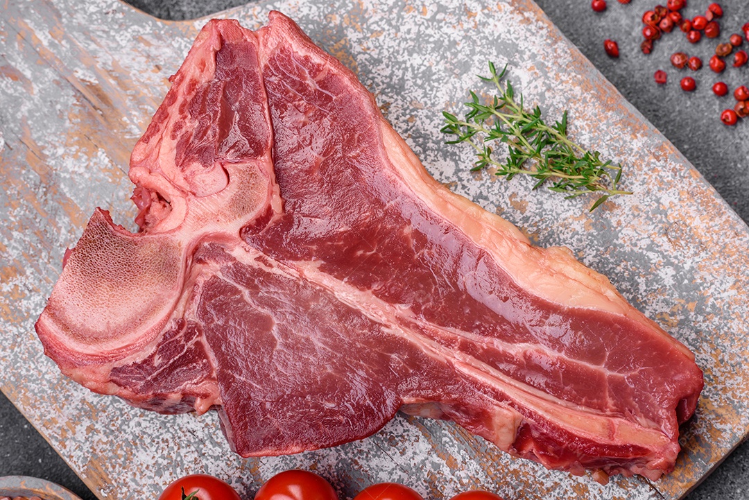 Bife de carne crua e suculenta com sal, especiarias e ervas sobre um fundo escuro de concreto