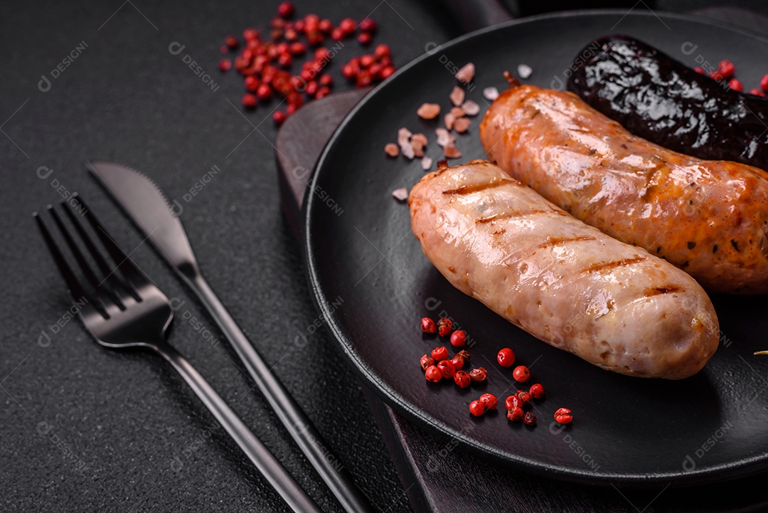 Deliciosas salsichas suculentas de diversas variedades grelhadas com sal, especiarias e ervas sobre um fundo escuro de concreto