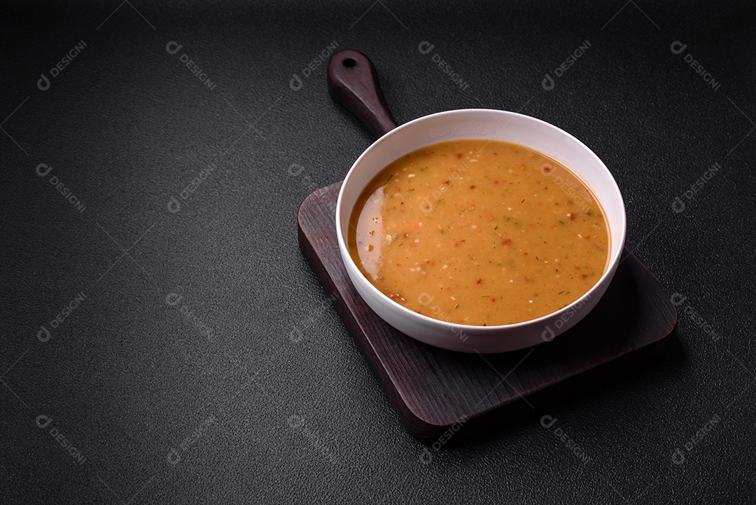 Deliciosa sopa de legumes frescos com cenouras, pimentões, batatas e cebolas em uma placa de cerâmica branca sobre um fundo escuro de concreto