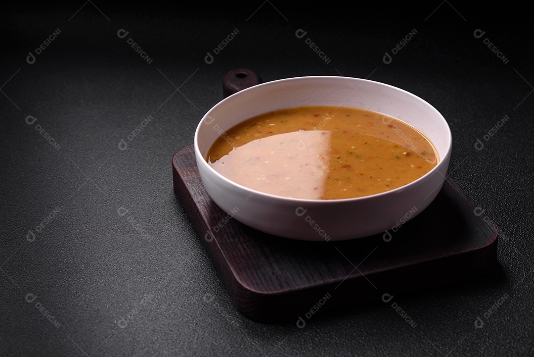 Deliciosa sopa de legumes frescos com cenouras, pimentões, batatas e cebolas em uma placa de cerâmica branca sobre um fundo escuro de concreto