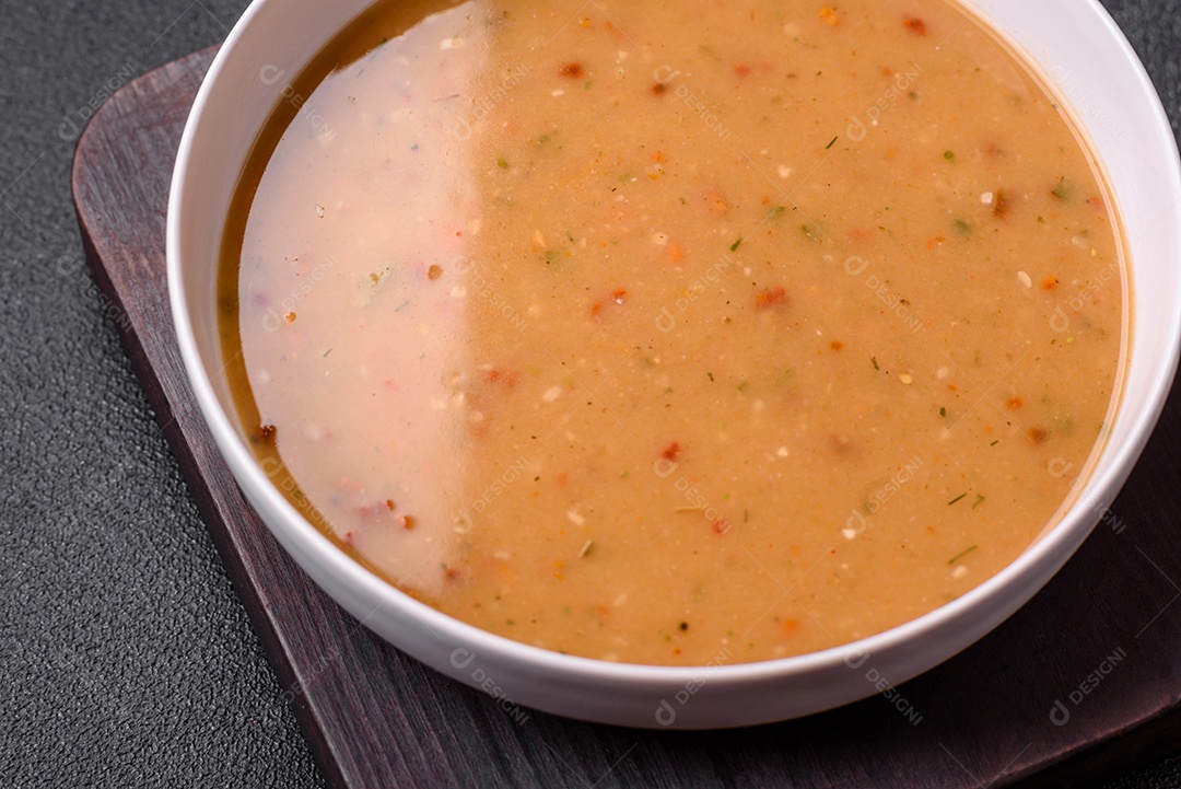 Deliciosa sopa de legumes frescos com cenouras, pimentões, batatas e cebolas em uma placa de cerâmica branca sobre um fundo escuro de concreto