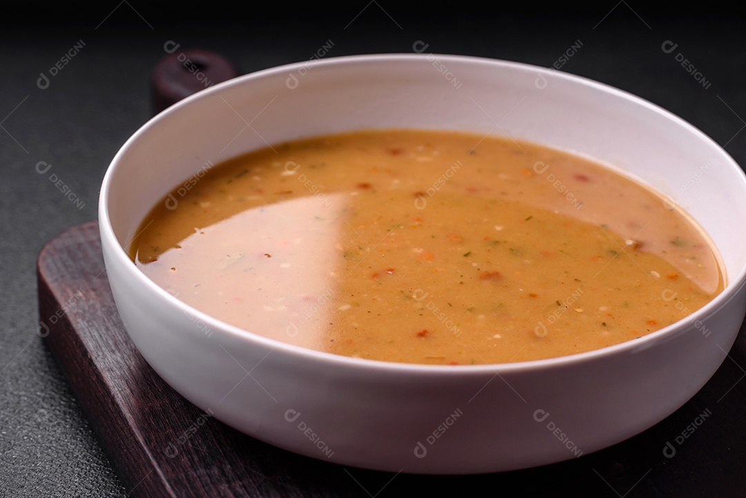 Deliciosa sopa de legumes frescos com cenouras, pimentões, batatas e cebolas em uma placa de cerâmica branca sobre um fundo escuro de concreto