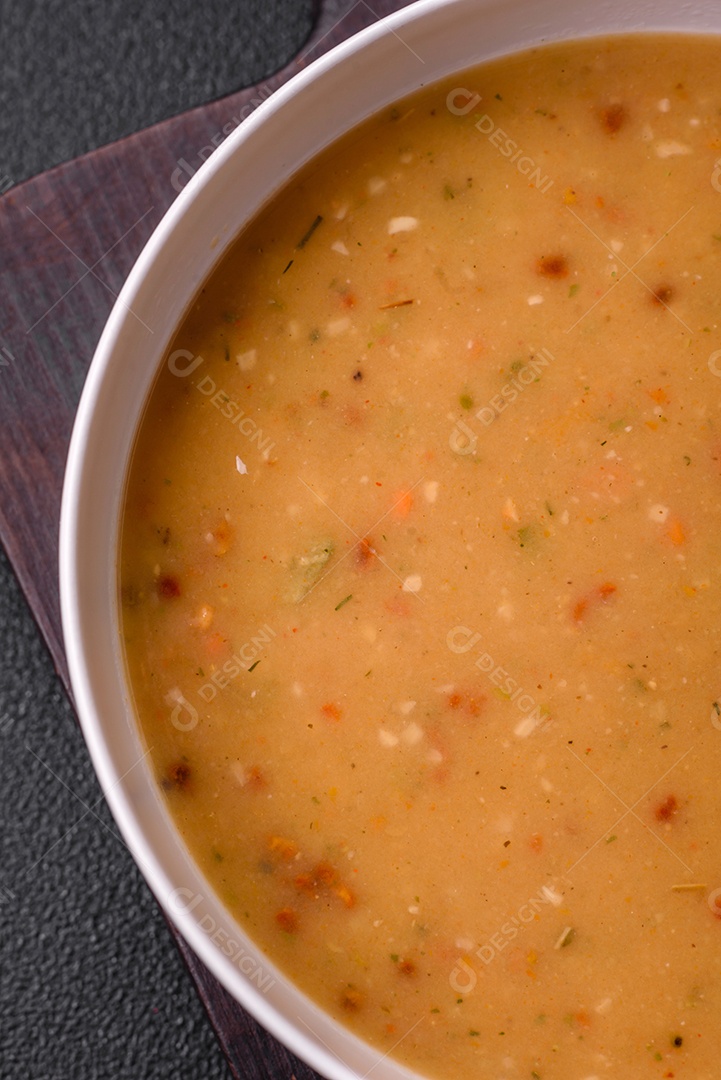 Deliciosa sopa de legumes frescos com cenouras, pimentões, batatas e cebolas em uma placa de cerâmica branca sobre um fundo escuro de concreto