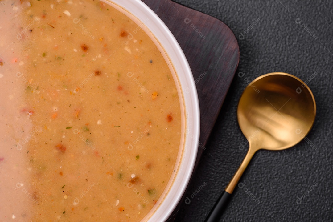 Deliciosa sopa de legumes frescos com cenouras, pimentões, batatas e cebolas em uma placa de cerâmica branca sobre um fundo escuro de concreto