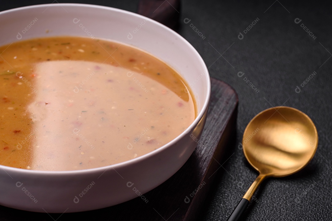 Deliciosa sopa de legumes frescos com cenouras, pimentões, batatas e cebolas em uma placa de cerâmica branca sobre um fundo escuro de concreto