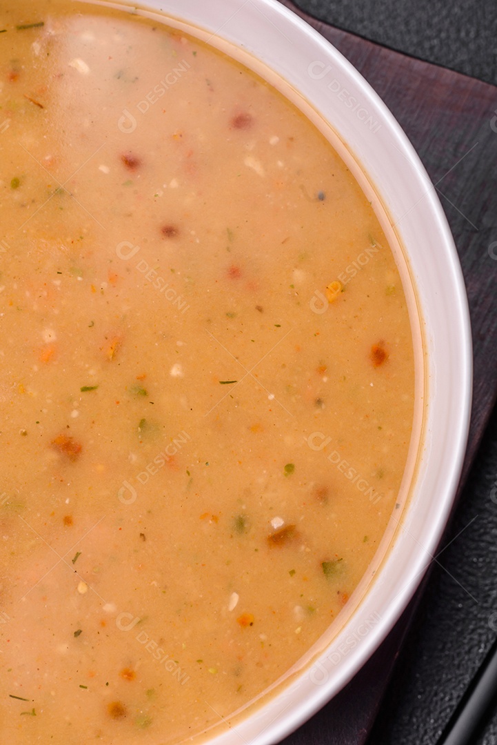 Deliciosa sopa de legumes frescos com cenouras, pimentões, batatas e cebolas em uma placa de cerâmica branca sobre um fundo escuro de concreto