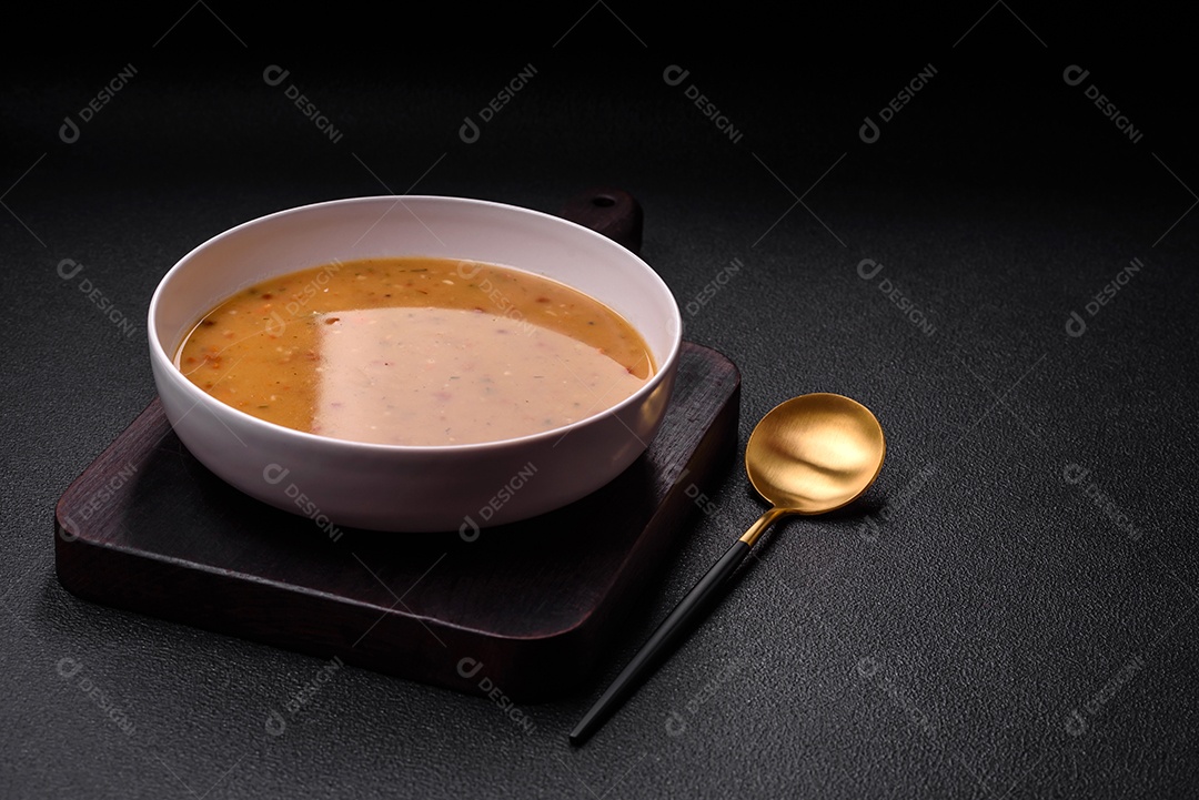 Deliciosa sopa de legumes frescos com cenouras, pimentões, batatas e cebolas em uma placa de cerâmica branca sobre um fundo escuro de concreto
