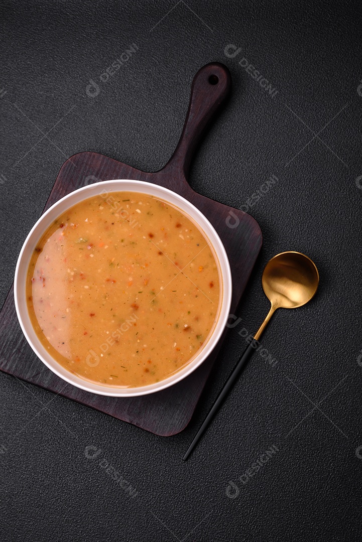 Deliciosa sopa de legumes frescos com cenouras, pimentões, batatas e cebolas em uma placa de cerâmica branca sobre um fundo escuro de concreto