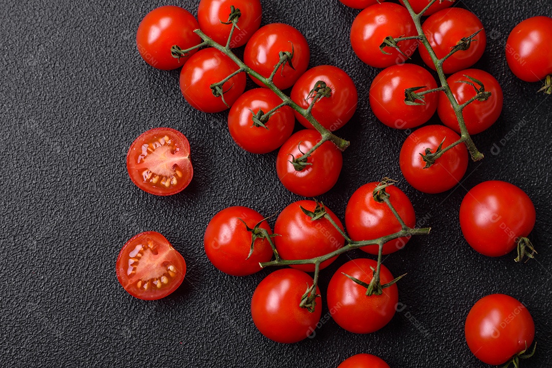 Deliciosos tomates cereja frescos nos galhos como ingrediente para cozinhar um prato vegetariano sobre um fundo escuro de concreto