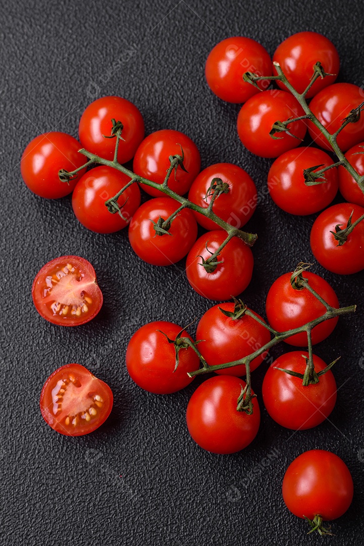Deliciosos tomates cereja frescos nos galhos como ingrediente para cozinhar um prato vegetariano sobre um fundo escuro de concreto