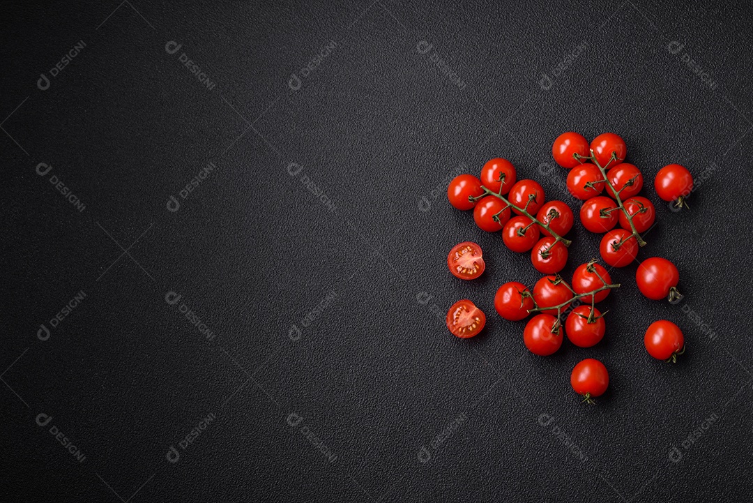 Deliciosos tomates cereja frescos nos galhos como ingrediente para cozinhar um prato vegetariano sobre um fundo escuro de concreto