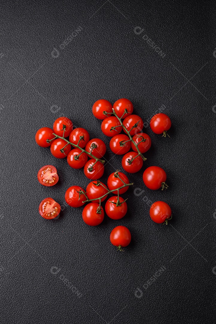 Deliciosos tomates cereja frescos nos galhos como ingrediente para cozinhar um prato vegetariano sobre um fundo escuro de concreto