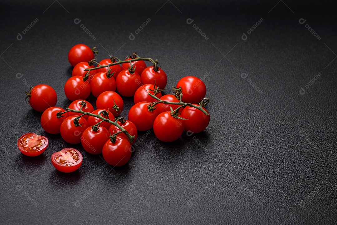 Deliciosos tomates cereja frescos nos galhos como ingrediente para cozinhar um prato vegetariano sobre um fundo escuro de concreto