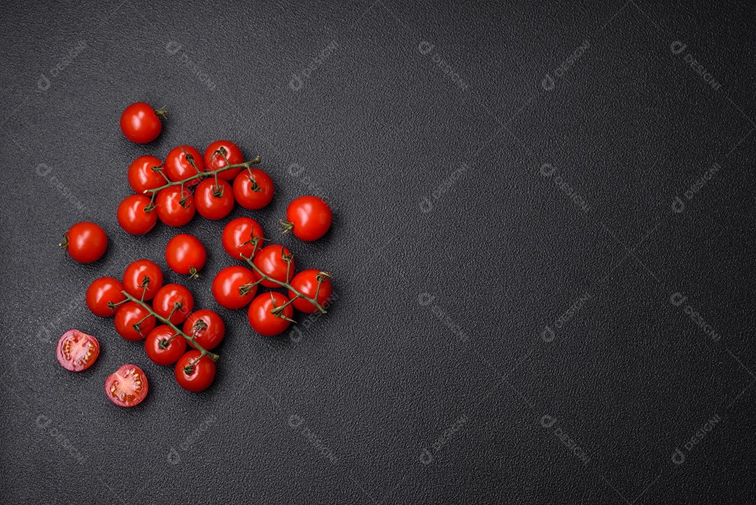 Deliciosos tomates cereja frescos nos galhos como ingrediente para cozinhar um prato vegetariano sobre um fundo escuro de concreto