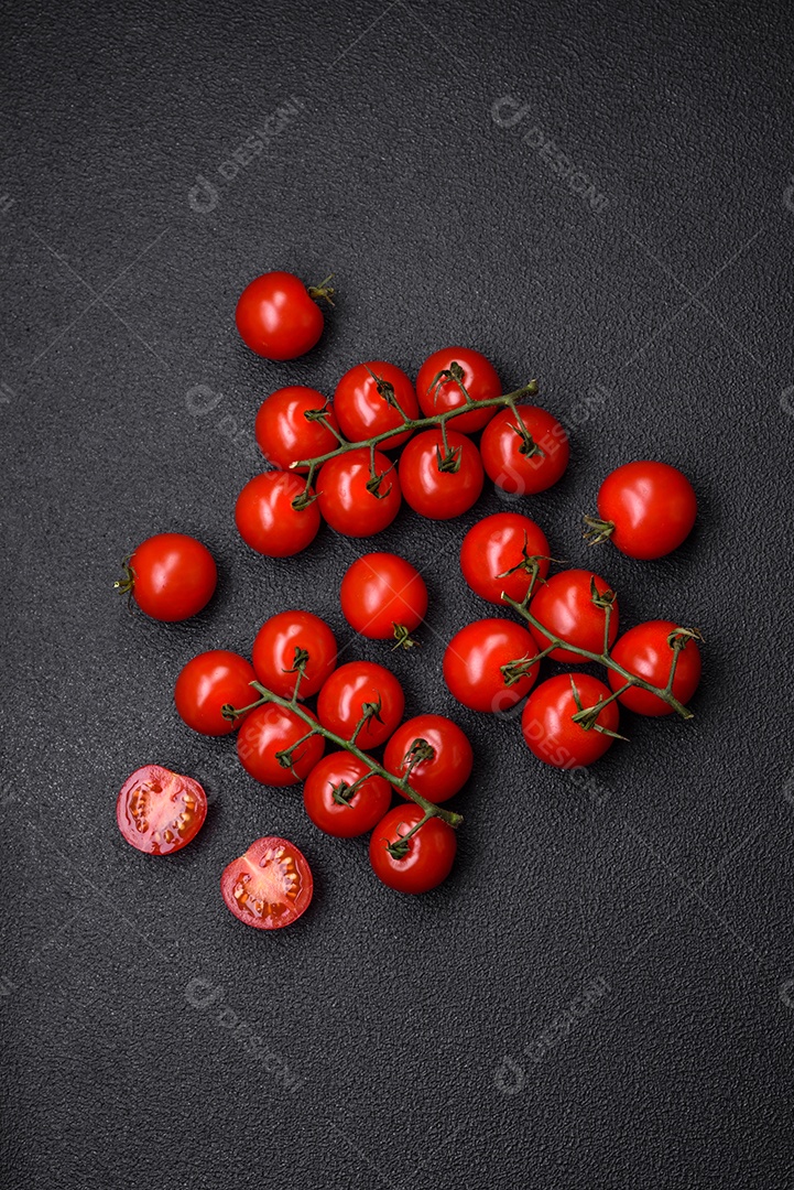 Deliciosos tomates cereja frescos nos galhos como ingrediente para cozinhar um prato vegetariano sobre um fundo escuro de concreto