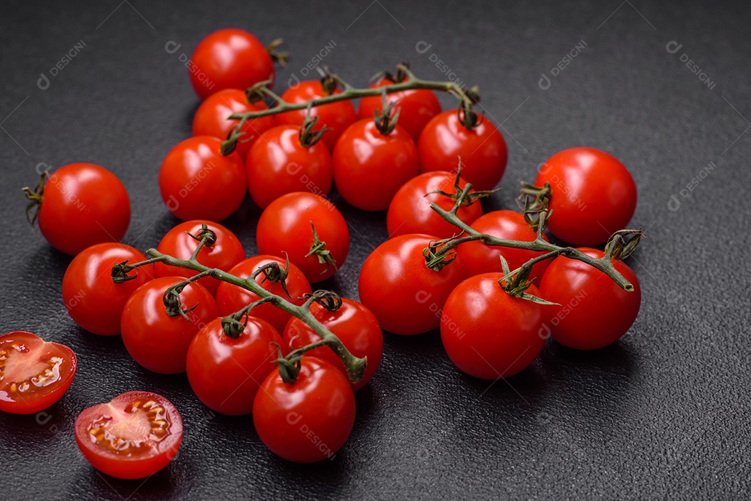 Deliciosos tomates cereja frescos nos galhos como ingrediente para cozinhar um prato vegetariano sobre um fundo escuro de concreto