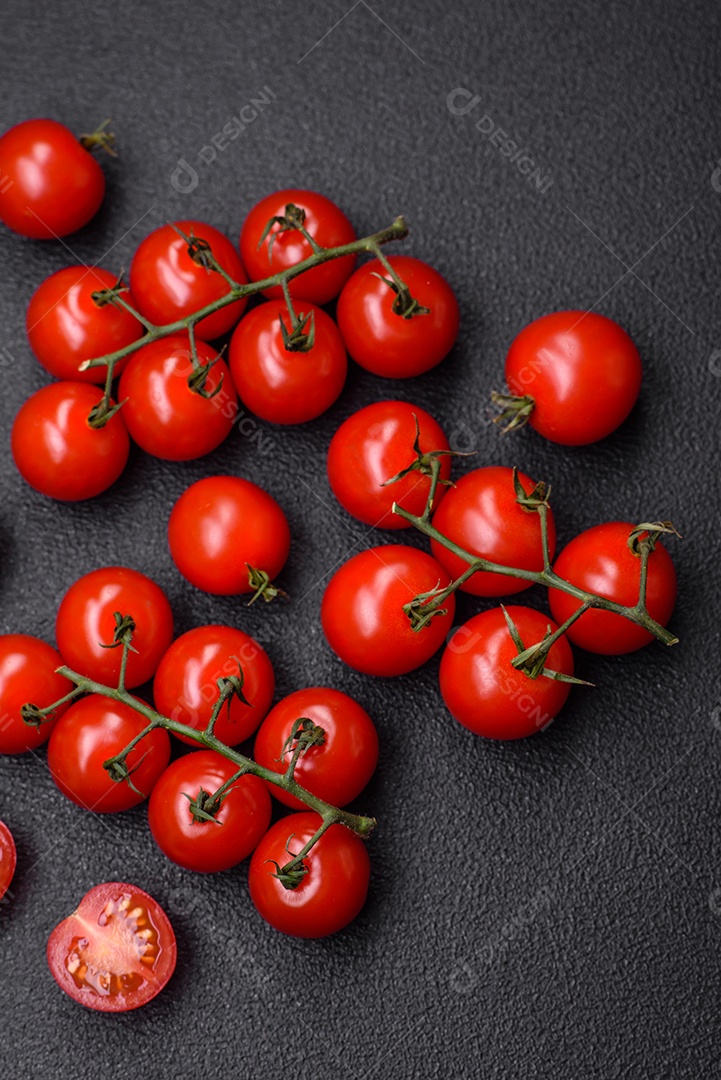 Deliciosos tomates cereja frescos nos galhos como ingrediente para cozinhar um prato vegetariano sobre um fundo escuro de concreto