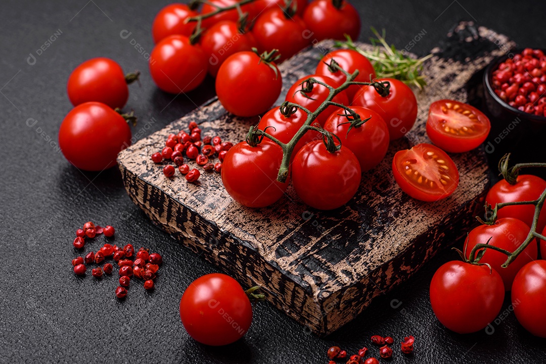 Deliciosos tomates cereja frescos nos galhos como ingrediente para cozinhar um prato vegetariano sobre um fundo escuro de concreto