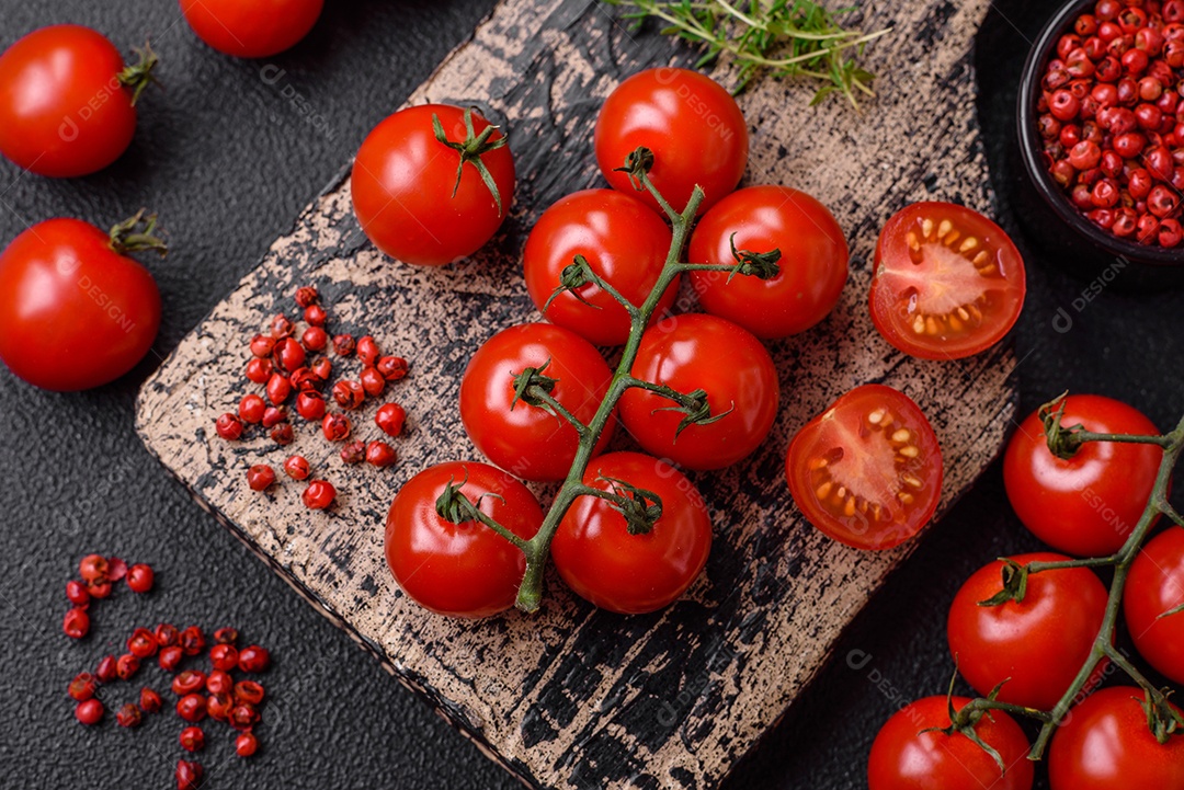 Deliciosos tomates cereja frescos nos galhos como ingrediente para cozinhar um prato vegetariano sobre um fundo escuro de concreto