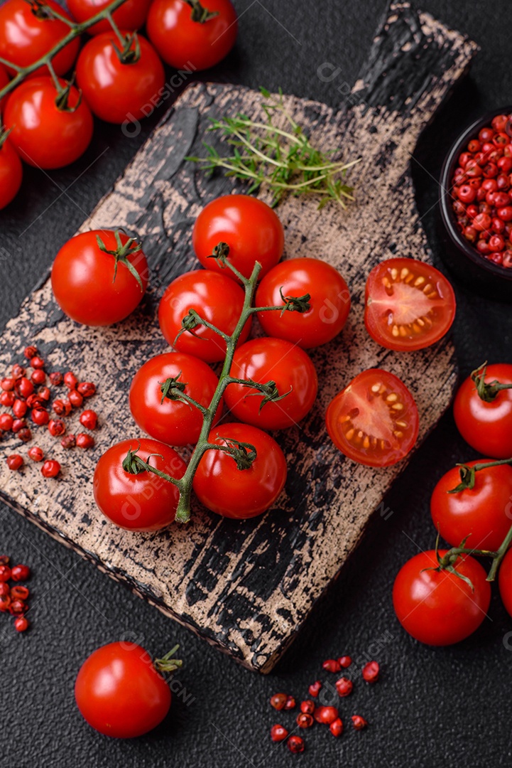 Deliciosos tomates cereja frescos nos galhos como ingrediente para cozinhar um prato vegetariano sobre um fundo escuro de concreto