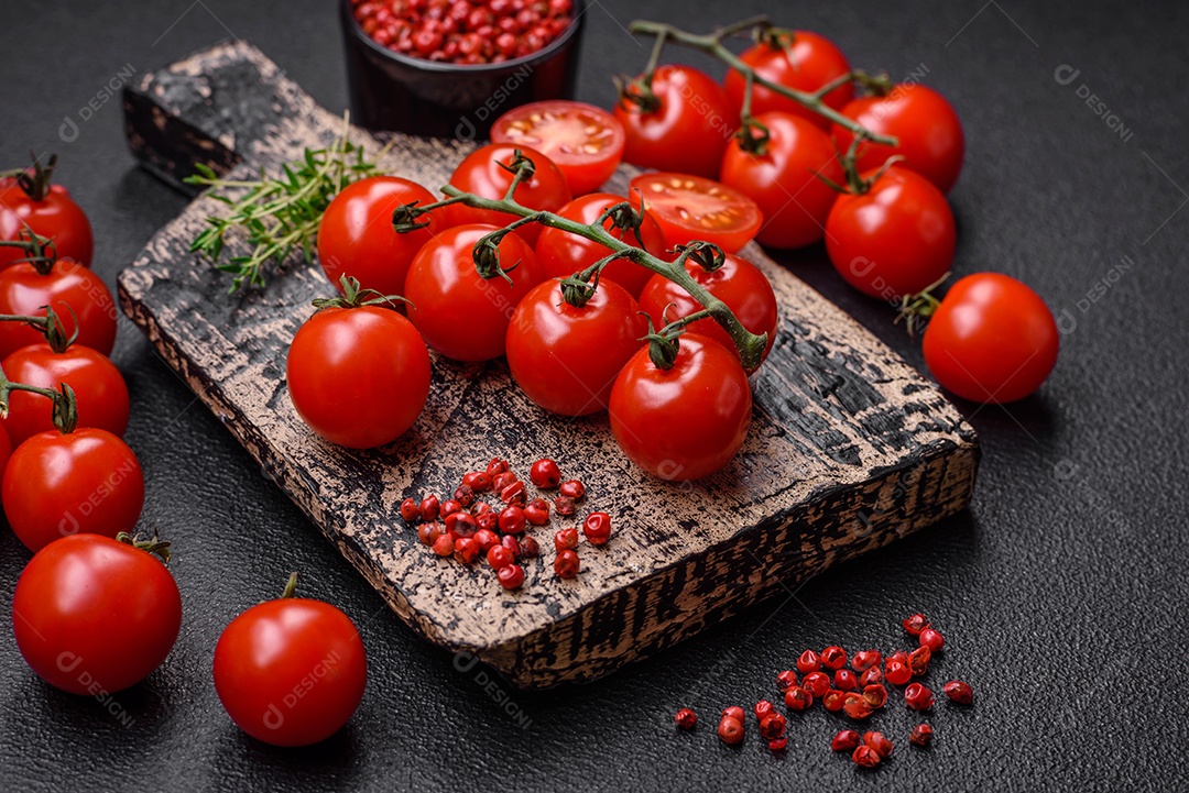 Deliciosos tomates cereja frescos nos galhos como ingrediente para cozinhar um prato vegetariano sobre um fundo escuro de concreto