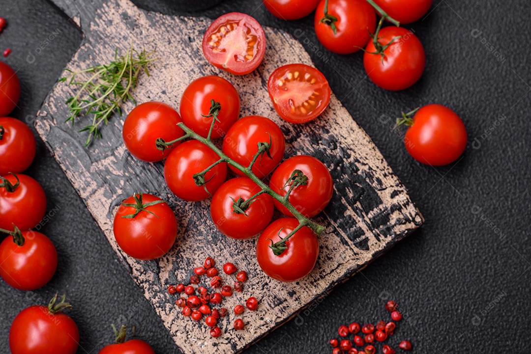 Deliciosos tomates cereja frescos nos galhos como ingrediente para cozinhar um prato vegetariano sobre um fundo escuro de concreto