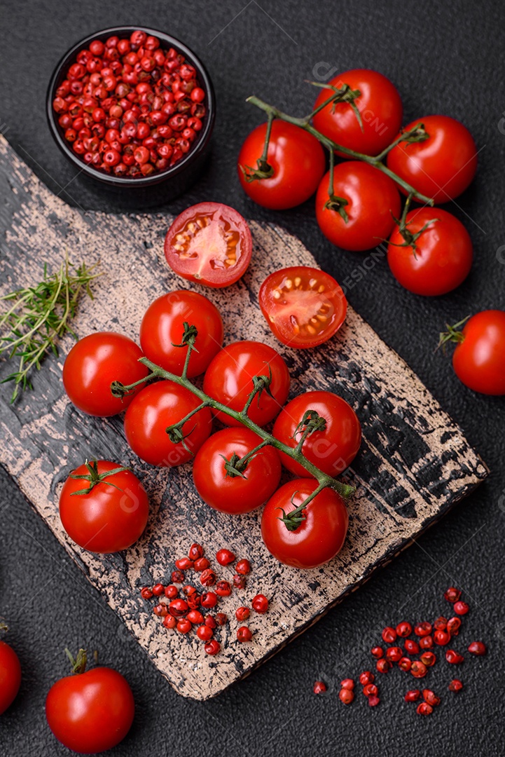 Deliciosos tomates cereja frescos nos galhos como ingrediente para cozinhar um prato vegetariano sobre um fundo escuro de concreto