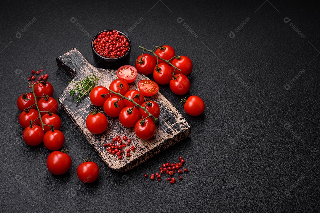 Deliciosos tomates cereja frescos nos galhos como ingrediente para cozinhar um prato vegetariano sobre um fundo escuro de concreto